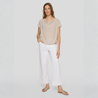 Woman wearing a beige top and white pants on a light gray background