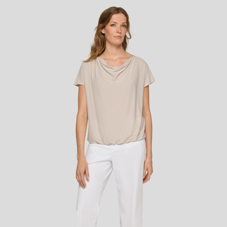 Woman wearing a beige top and white pants against a plain background