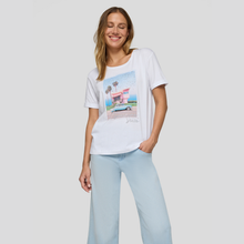 Load image into Gallery viewer, Woman wearing a white t-shirt with a graphic design and light blue pants on a plain background

