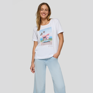 Woman wearing a white t-shirt with a graphic design and light blue pants on a plain background