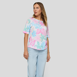 Woman wearing a pastel floral top and light blue pants on a plain background