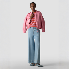 Load image into Gallery viewer, Person wearing a pink jacket, striped shirt, and blue jeans on a light gray background

