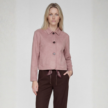 Load image into Gallery viewer, A woman modeling a dusty pink cropped suede jacket with three dark buttons and a pointed collar, paired with dark brown trousers, against a light gray textured studio background.
