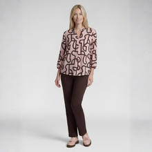 Load image into Gallery viewer, A woman modeling a three-quarter sleeve blouse with an abstract brown line pattern on a dusty pink background, paired with dark brown pants and pink shoes, against a light gray studio background.
