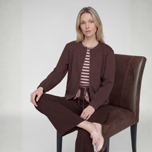 Load image into Gallery viewer, A woman sits on a brown upholstered chair wearing a coordinated brown outfit consisting of a cropped long-sleeve cardigan, striped top, and matching pants, against a plain light gray studio background.
