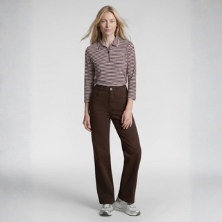 A woman modeling a brown and white horizontally striped long-sleeve polo shirt paired with dark brown wide-leg trousers and light gray sneakers, set against a plain light gray studio background.