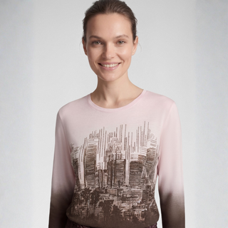 A woman wearing a sheer long-sleeve top with a gradient color transition from pale pink at the shoulders to dark brown at the hem, featuring a black and white cityscape graphic print across the front.