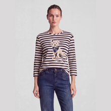 Load image into Gallery viewer, A woman modeling a navy and beige striped long-sleeve top with a detailed kitten graphic on the front, paired with dark blue jeans, against a light gray studio background.
