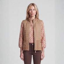 Load image into Gallery viewer, A woman modeling a tan quilted zip-front vest over a beige and red patterned blouse, paired with dark brown pants, against a light gray studio background.
