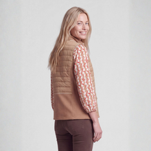 Load image into Gallery viewer, A woman wearing a tan quilted sleeveless vest over a long-sleeve patterned blouse with brown pants, photographed against a plain light gray studio background.
