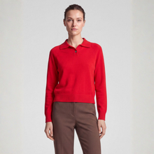 Load image into Gallery viewer, A woman modeling a bright red knit polo sweater with a collar and button placket, paired with brown trousers, against a plain light gray studio background.
