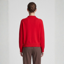 Load image into Gallery viewer, A model viewed from the back wearing a bright red knit sweater with a mock neck and brown trousers, set against a plain light gray studio background.
