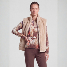 Load image into Gallery viewer, A woman modeling a beige sherpa-lined zip-front vest over a brown and beige abstract-print long-sleeve top, paired with brown pants, against a light gray studio background.
