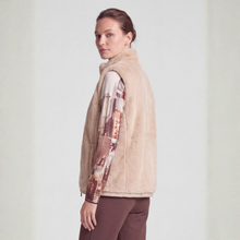 Load image into Gallery viewer, A woman wearing a beige sherpa fleece vest over a long-sleeve shirt with a brown and beige cityscape print, paired with brown pants, photographed against a light gray studio background.
