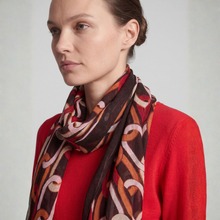 Load image into Gallery viewer, A woman wearing a red top and a patterned scarf with abstract swirls in brown, orange, beige, and white, photographed against a light gray studio background.
