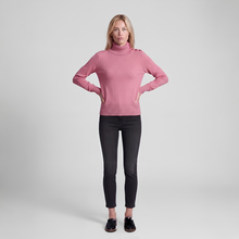 Load image into Gallery viewer, A woman modeling a pink long-sleeve turtleneck sweater with shoulder details, paired with black skinny jeans and black shoes, against a light gray studio background.
