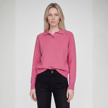 Load image into Gallery viewer, A woman modeling a pink knit polo sweater with a collar and short button placket, paired with black jeans, against a plain light gray studio background.
