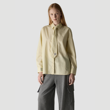 Load image into Gallery viewer, A model wearing a pale yellow pinstriped long-sleeve shirt with a matching tie-neck detail and gray pinstriped cargo pants, set against a plain light gray studio background.
