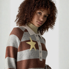 Load image into Gallery viewer, A woman with curly brown hair wearing a brown and gray striped knit polo sweater with a yellow star detail on the chest, photographed against a light neutral background.
