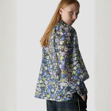 Load image into Gallery viewer, A model with long red hair is shown from a side-back angle wearing a dark floral print shirt with blue, green, and white flowers, paired with dark plaid trousers against a plain light background.
