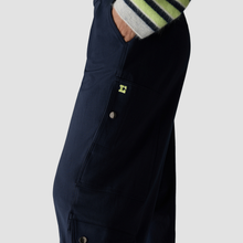 Load image into Gallery viewer, Close-up of a person wearing dark navy overalls with a striped knit sweater visible at the cuff, against a light gray studio background.
