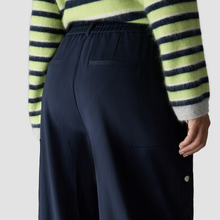 Load image into Gallery viewer, Close-up back view of a person wearing dark navy wide-leg trousers and a fuzzy striped sweater with lime green, navy, and white horizontal stripes, against a light gray studio background.
