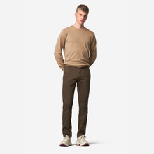 Load image into Gallery viewer, A male model stands against a light gray studio background wearing a tan long-sleeve crewneck shirt, dark brown pants, a patterned belt, and off-white sneakers.
