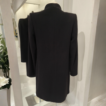 Load image into Gallery viewer, A black longline coat displayed on a mannequin from the back, with a mirror reflecting the side view in a bright indoor setting.
