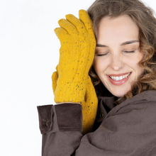 Load image into Gallery viewer, A smiling woman with closed eyes wearing a pair of mustard yellow knit gloves with small dark speckles, posed against a clean white background.

