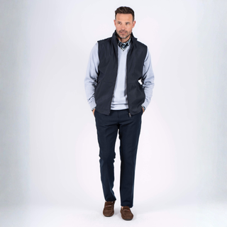 Man wearing a dark vest over a light shirt with dark pants on a white background