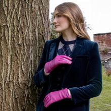 Load image into Gallery viewer, A woman wearing a dark navy velvet blazer, argyle sweater, and bright pink leather gloves, standing outdoors next to a large textured tree trunk.
