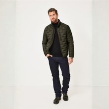 Load image into Gallery viewer, A man wearing a dark olive green quilted puffer jacket over a black turtleneck sweater, dark blue jeans, and black shoes, standing against a plain white studio background.
