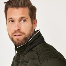 Load image into Gallery viewer, A close-up shot of a man wearing an olive green puffer jacket with a high collar, set against a plain light gray background.
