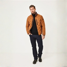 Load image into Gallery viewer, A man wearing a brown quilted puffer jacket over a black turtleneck sweater, dark blue jeans, and black shoes, standing against a plain white studio background.
