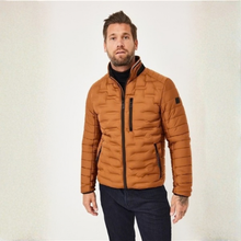 Load image into Gallery viewer, A man wearing a quilted brown puffer jacket with black trim, a black turtleneck, and dark blue jeans, standing against a light textured studio background.
