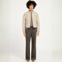 Load image into Gallery viewer, A model stands against a plain white studio background wearing a light beige cropped jacket over a brown and beige striped shirt, paired with dark gray wide-leg trousers.
