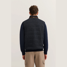 Load image into Gallery viewer, Man wearing a dark blue sweater vest over a black shirt with beige pants on a light gray background
