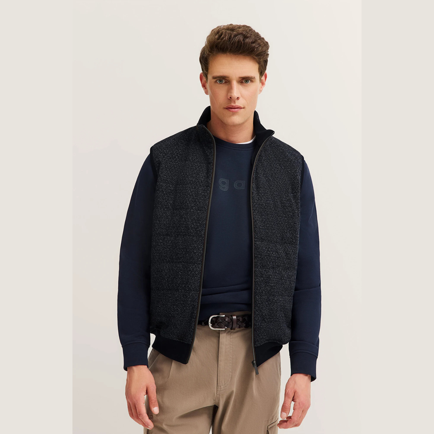 Man wearing a dark blue sweater with a vest over it on a plain background