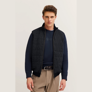 Man wearing a dark blue sweater with a vest over it on a plain background