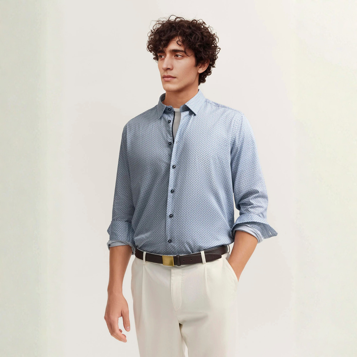 Man wearing a blue patterned shirt and white pants against a light background