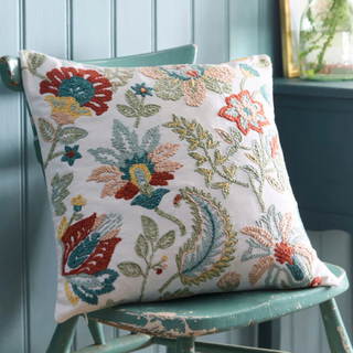 Decorative pillow with floral embroidery on a green chair against a blue wall.