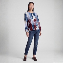 Load image into Gallery viewer, A model stands against a light gray studio background wearing a long-sleeve abstract print top with blue, burgundy, white, and beige tones, paired with dark blue jeans and brown leather loafers.
