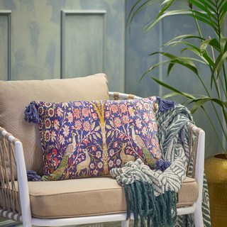Decorative pillow with floral pattern on a beige sofa with a green blanket, against a light blue wall.