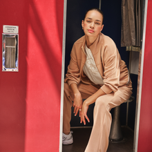 Load image into Gallery viewer, Woman sitting in a dressing room wearing a beige outfit.
