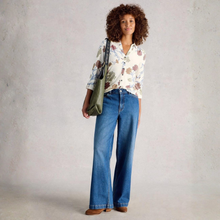 Load image into Gallery viewer, Woman wearing a floral blouse and blue jeans holding a green bag against a plain background
