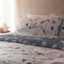 Load image into Gallery viewer, Floral patterned bedding set on a bed with pillows and a candle in the background.
