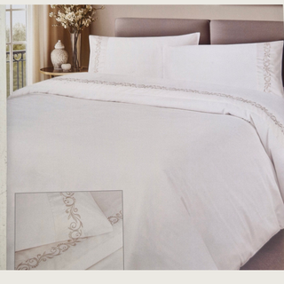 Champagne bedding set with decorative embroidery on a bed in a bedroom.