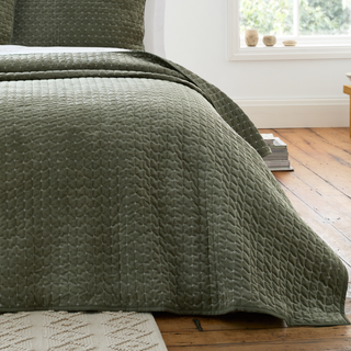 Green quilted cover on a bed in a room with wooden flooring and a window.