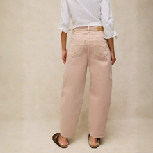 Load image into Gallery viewer, A person shown from the back wearing light blush pink wide-leg jeans, a white long-sleeve blouse, and brown flat sandals against a neutral beige studio backdrop.
