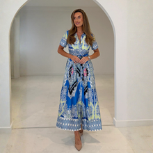 Load image into Gallery viewer, Woman wearing a blue and white patterned dress standing in a white archway.
